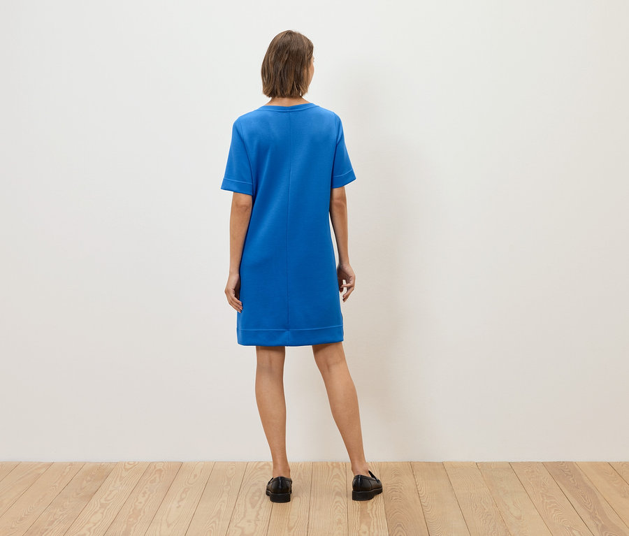 A nő háttal áll a kamerának, kék ruhát és fekete cipőt visel.