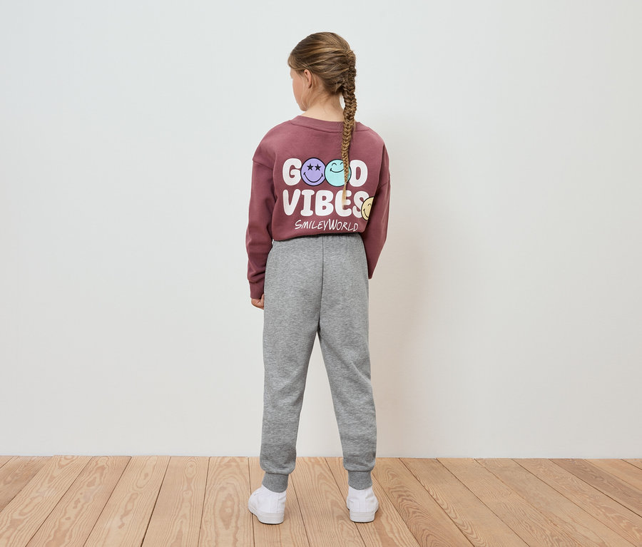 Egy lány hátulról látható, bordó pulóvert visel Good Vibes felirattal és szürke melegítőnadrágot.