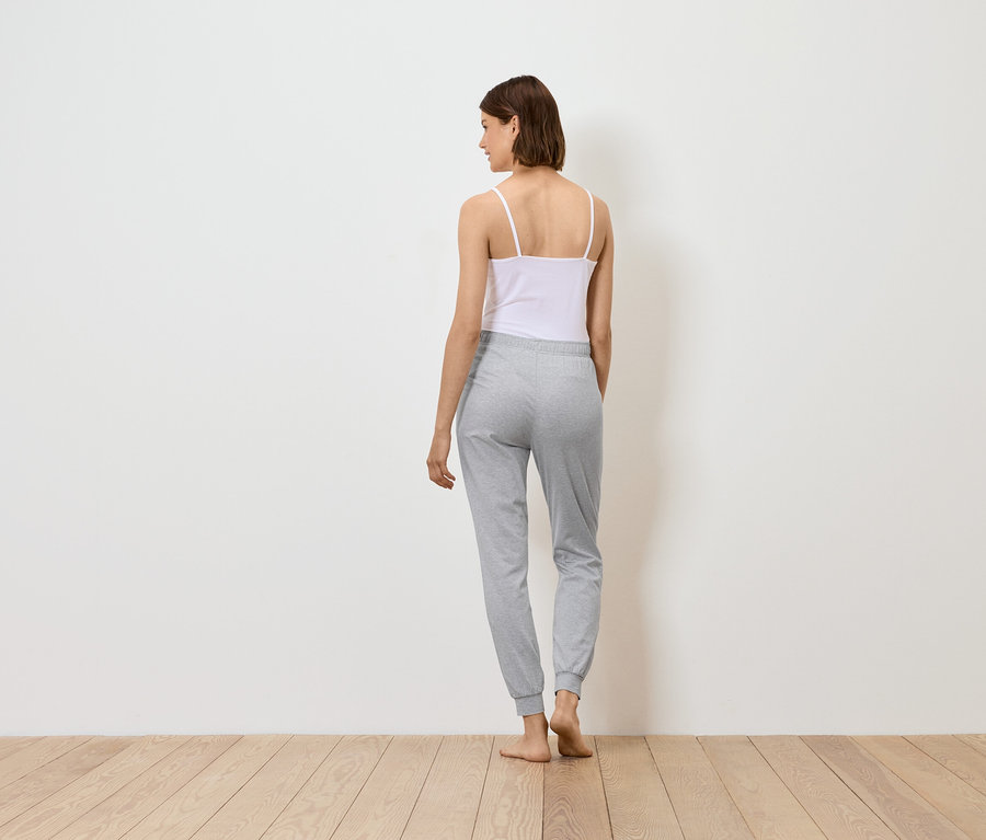 Egy nő háttal áll, fehér felsőt és szürke jogging alsót visel.