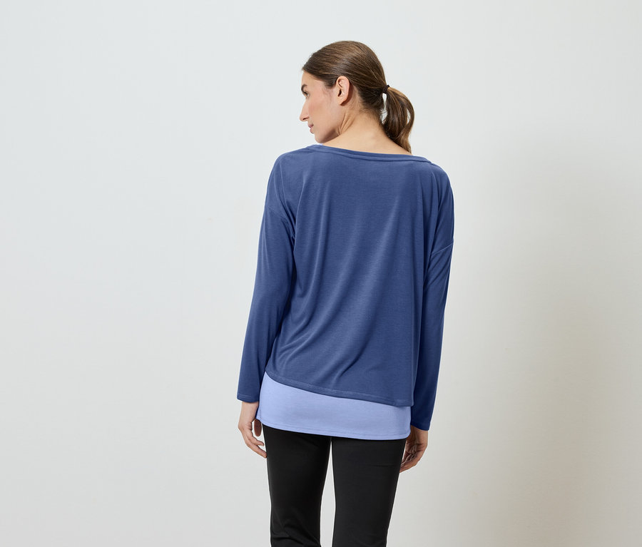 Egy nő háttal a kamerának kék hosszú ujjú inget és fekete nadrágot visel.