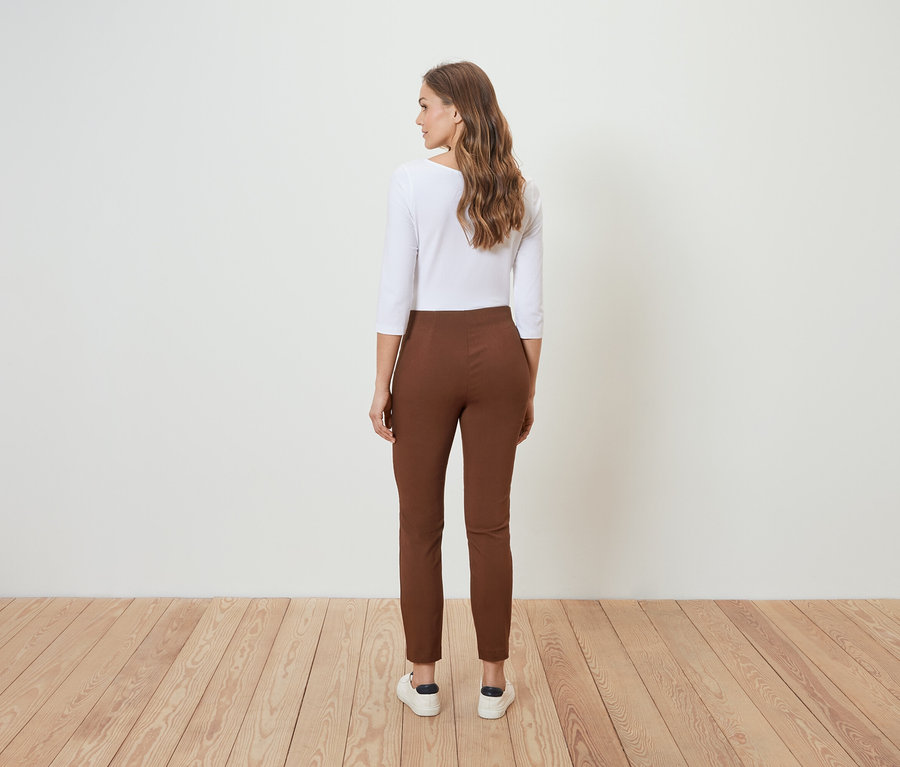 Egy nő háttal áll a kamerának, barna nadrágot és fehér blúzt visel.