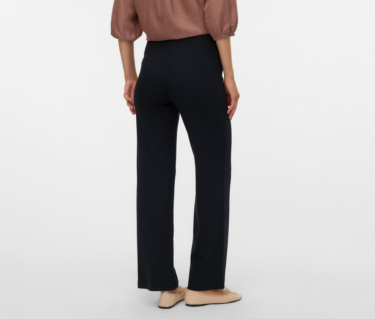 Hátulnézet egy barna blúzt, fekete MAMALICIOUS kismama leggingset és bézs balerinát viselő nőről.