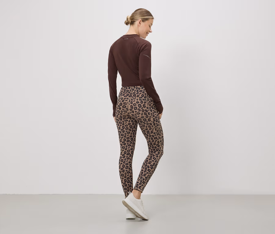 Egy nő hátulról, barna felsőben, leopárdmintás leggingsben és fehér tornacipőben.