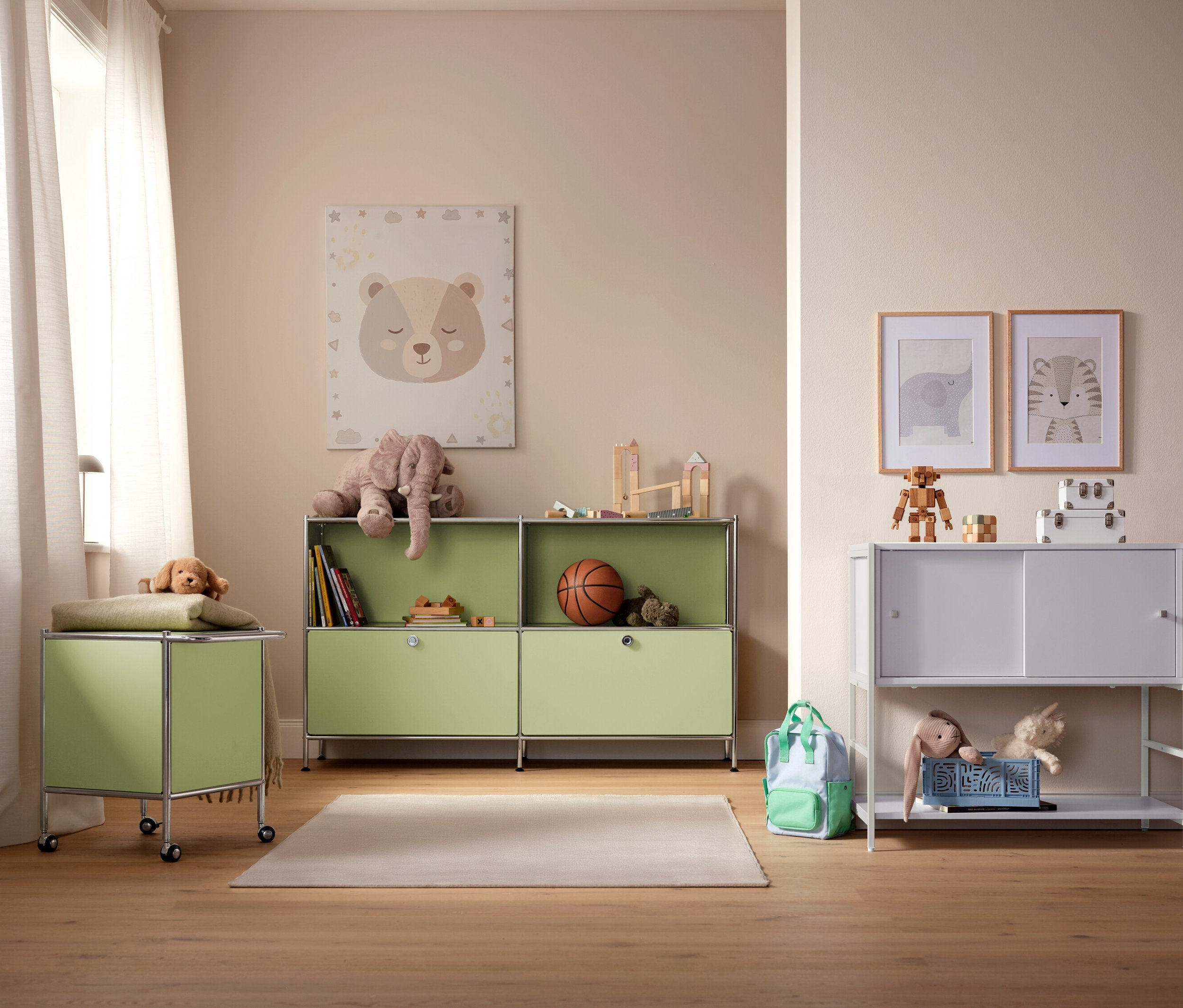 Gyerekszoba világoszöld és fehér tárolószekrényekkel, játékokkal és képekkel a falon.