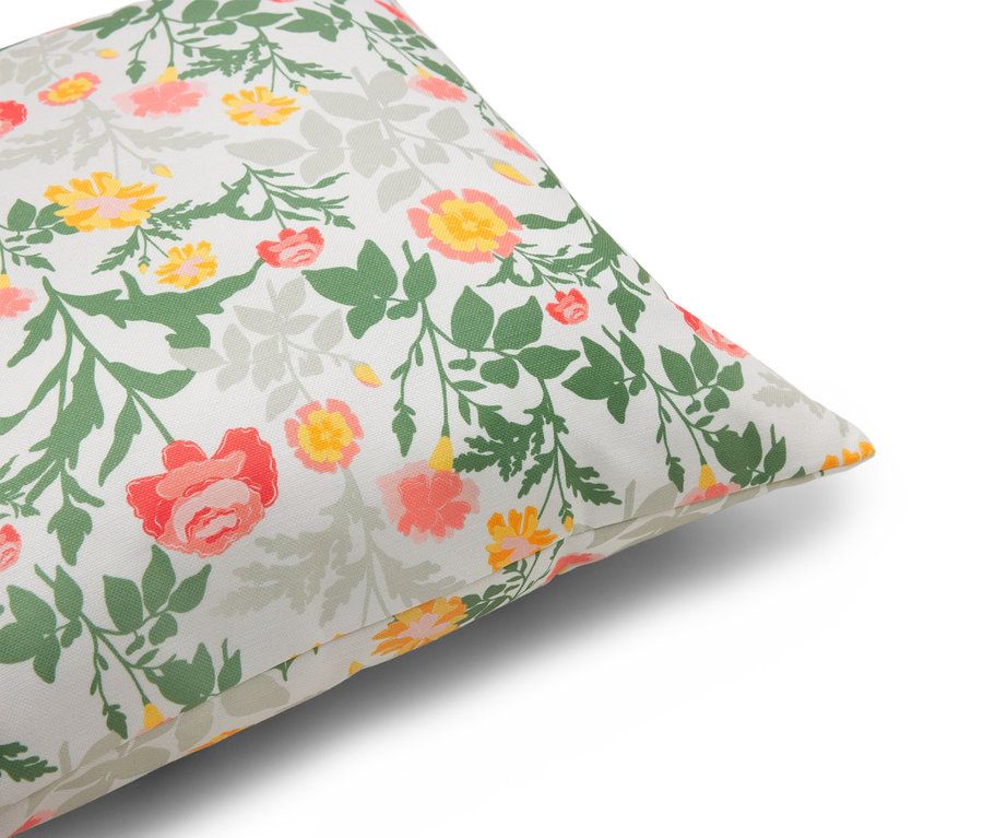 Egy párna közeli képe virágmintával piros, sárga és zöld színekben, fehér háttérrel.