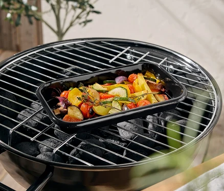 Zöldségek egy fekete tepsiben a grillen.