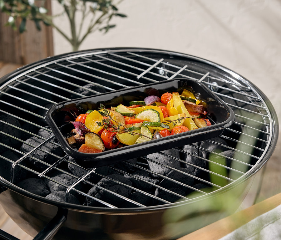 Zöldségek egy fekete tepsiben a grillen.
