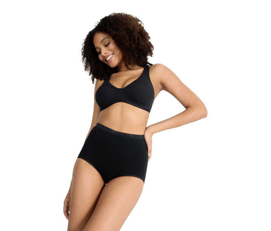 Göndör hajú nő fekete melltartót és fekete, magas derekú alsóneműt visel, enyhén lefelé nézve.