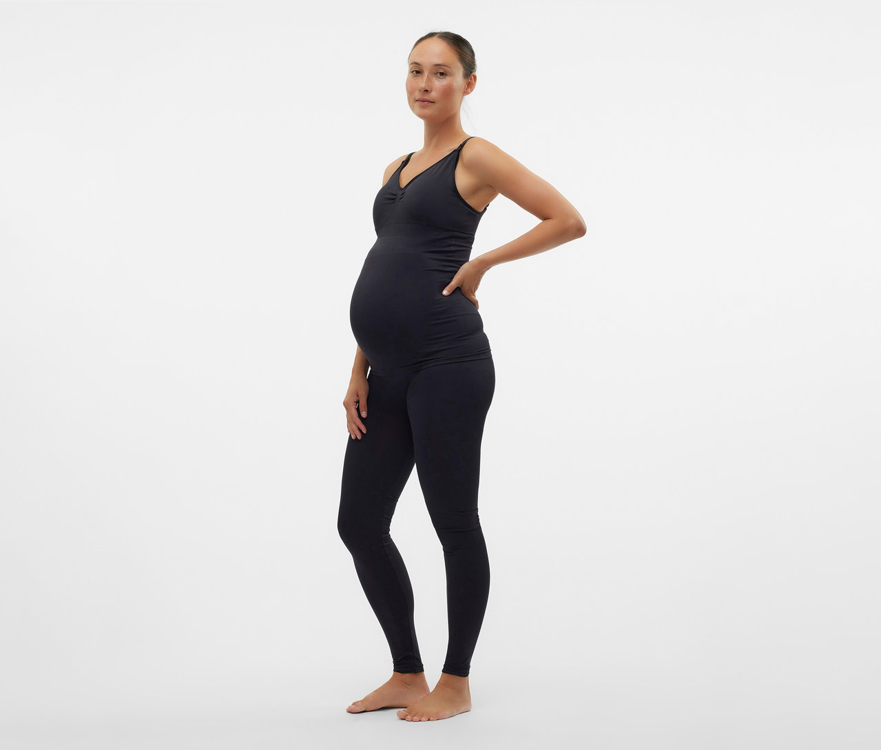 Fekete felsőt és MAMALICIOUS kismama leggingset viselő terhes nő oldalra pózol.