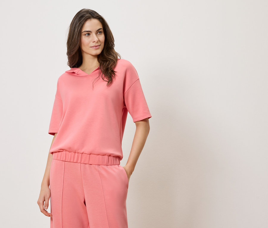 Nő visel rózsaszín, rövid ujjú kapucnis pulóvert és rózsaszín nadrágot.