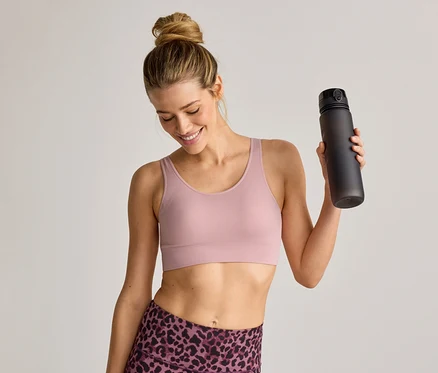 Sportmelltartót és leggingst viselő nő fekete kulacsot tart a kezében és mosolyog.