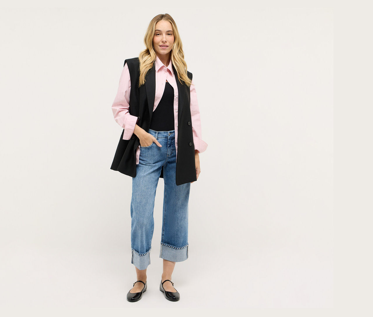 Nő fekete mellényben, rózsaszín ingben, farmerban és fekete cipőben.