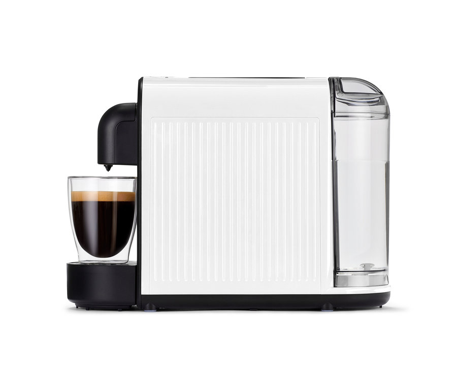 A fehér Cafissimo now white kávéfőző egy pohár tele kávéval az asztalon áll.