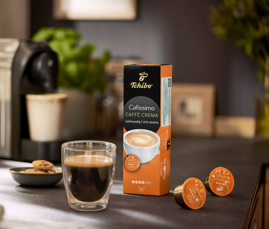 Kávéfőző egy csésze kávéval, kekszekkel és egy csomag Cafissimo Caffe Crema kapszulával.