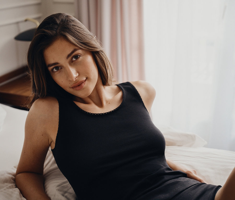 Egy nő portréja, aki fekete trikóban fekszik az ágyon.