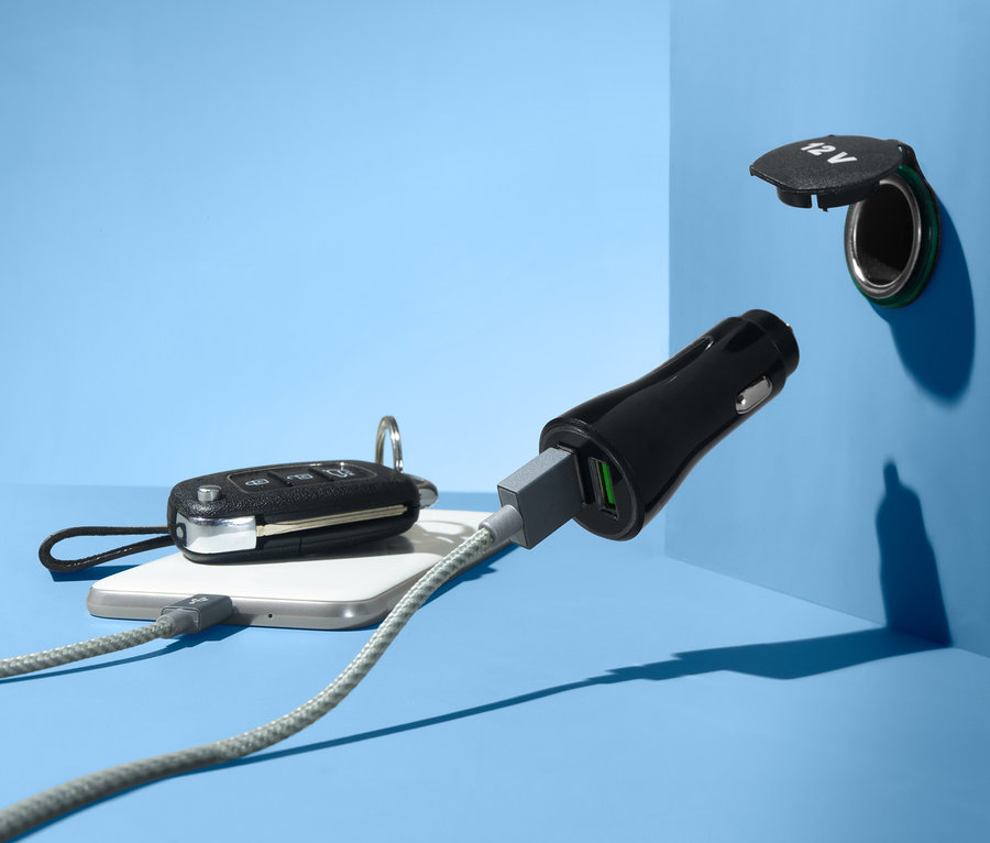 Kék háttér előtt egy autós USB töltő csatlakozik egy 12V-os aljzathoz. Egy kábel egy mobiltelefonhoz van csatlakoztatva.