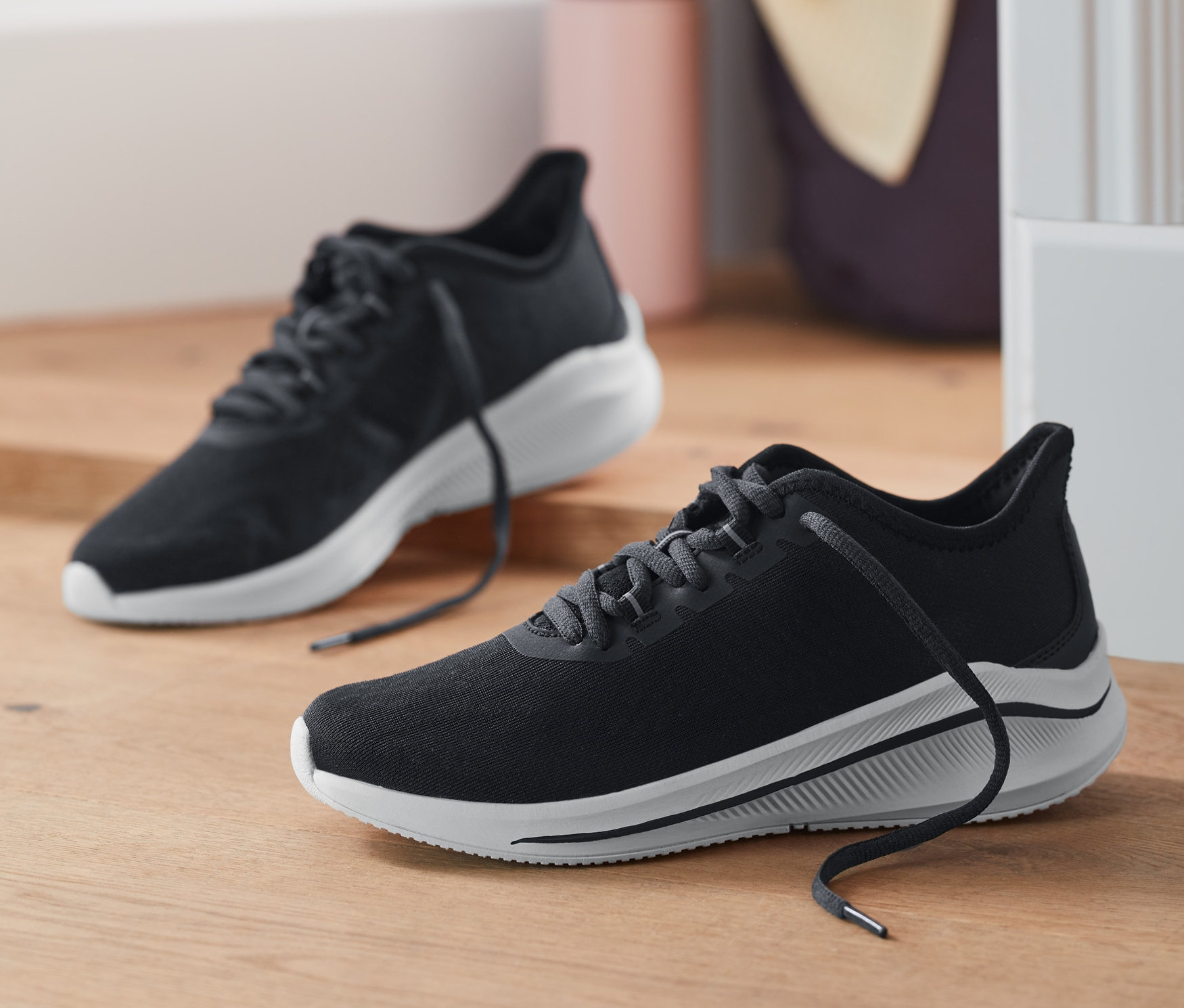 Két sneaker cipő van a fapadlón az ajtó mellett.