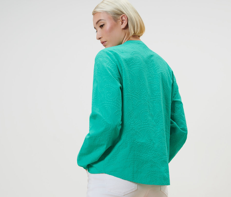 Nő pózol zöld, hímzett blúzban.
