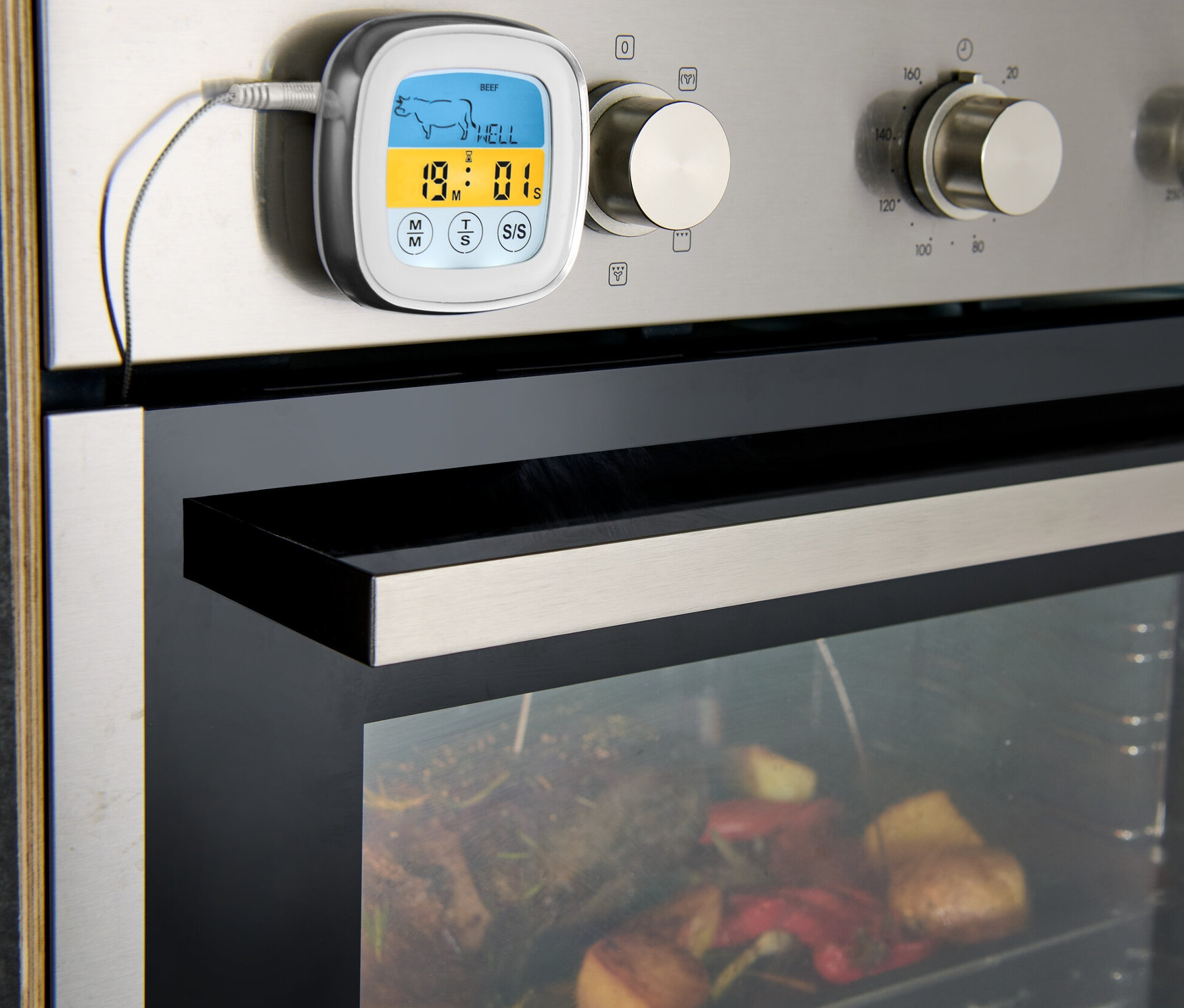 A sütőre rögzített maghőmérő, belül sült hús és zöldségek.