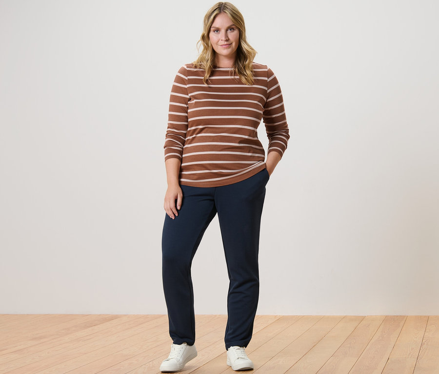 Nő pózol barna-krém csíkos hosszú ujjú felsőben és sötétkék női lezser nadrágban.