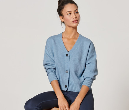 Egy nő ül egy széken és kék kötött kardigánt visel.