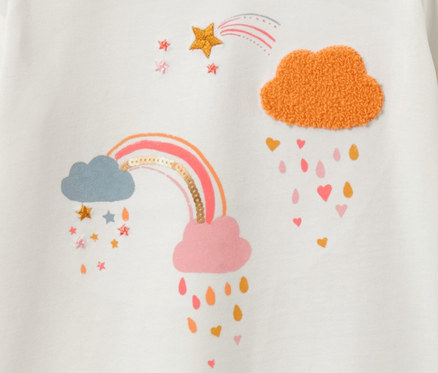 Egy fehér, szivárvány és felhő mintájú hosszú ujjú gyerekfelső részlete.