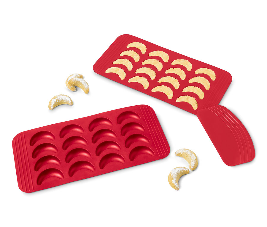 Két piros szilikon vaníliás kifli sütőforma, az egyik tele sült kiflikkel, a másik üres, és néhány kifli mellette.