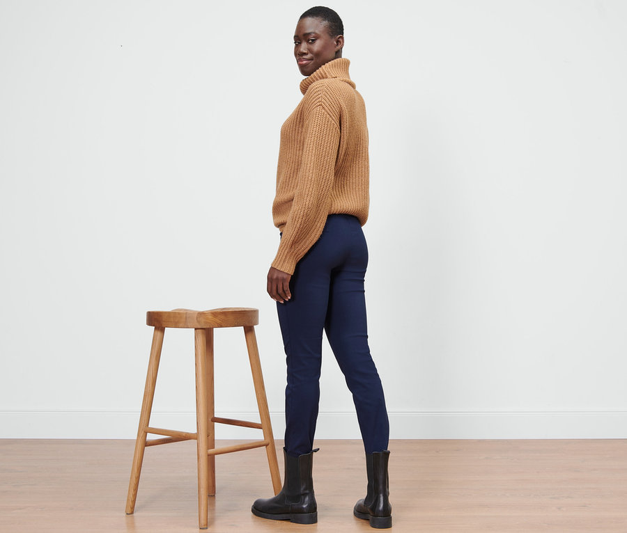 Egy nő egy szék mellett pózol, kék sztreccsnadrágot visel.