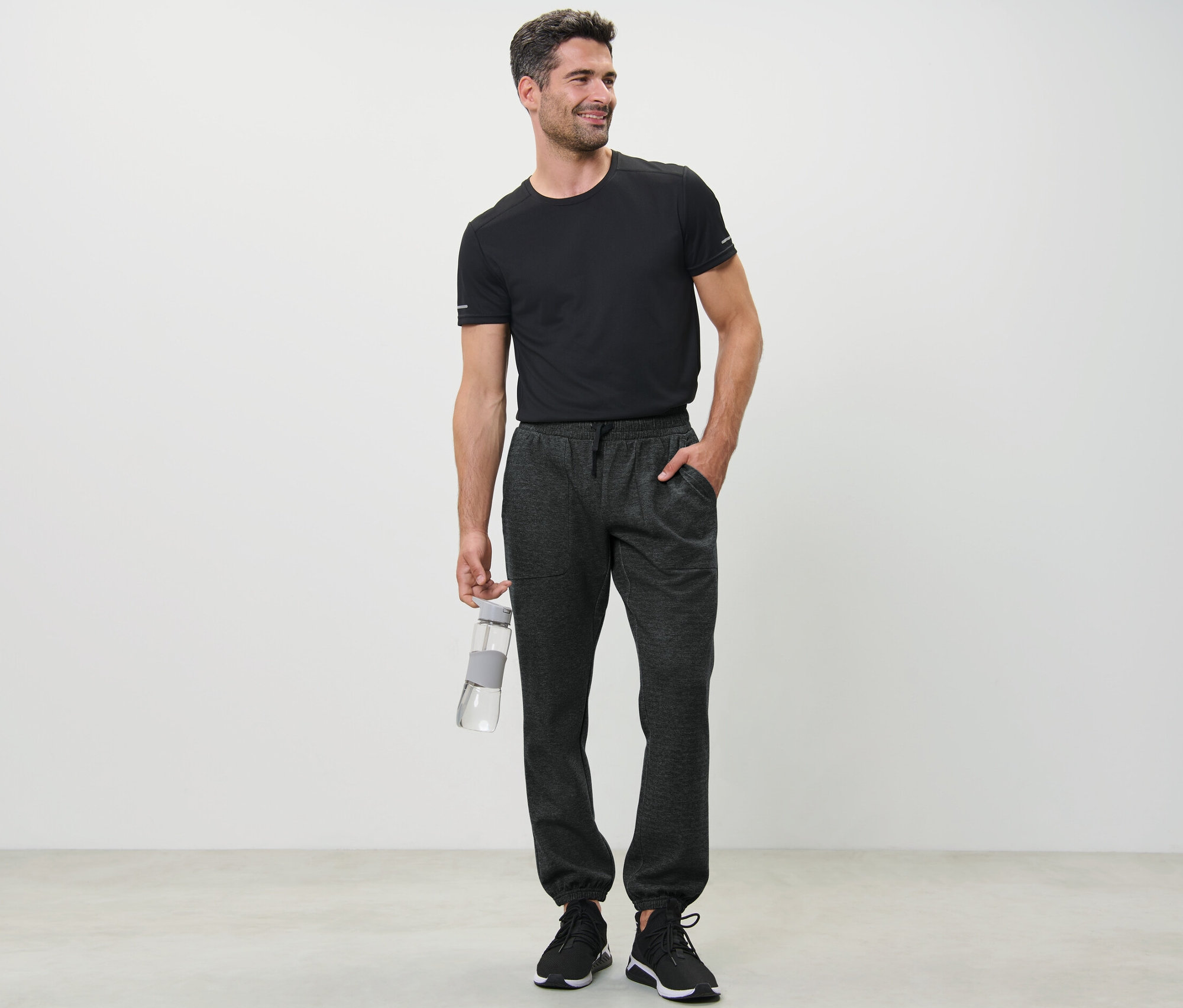 Férfi fekete pólóban vizet tart és funkcionális szabadidőnadrágot visel.