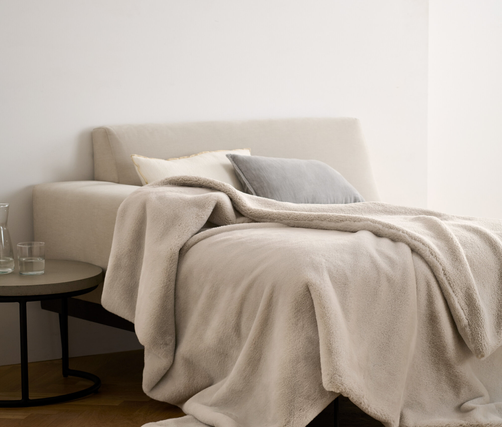 Egy bézs színű, puha takaró (130x170 cm) fekszik egy ágyon, párnákkal.