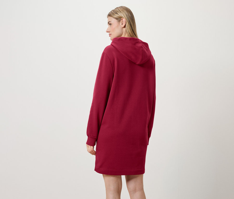 Egy nő háttal a kamerának, piros kapucnis pulóverruhát visel.