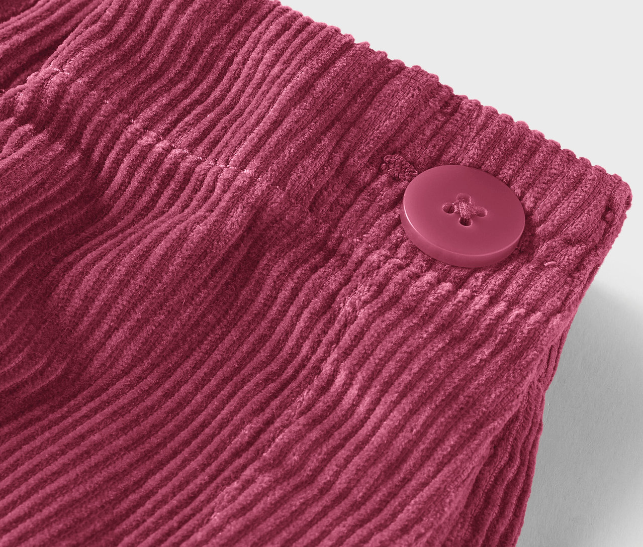 Egy bordó színű kordbársony anyag részlete gombbal.