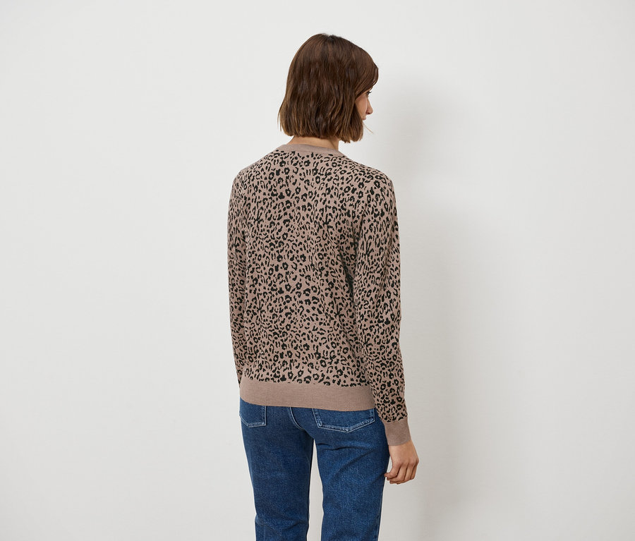 Hátulról egy rövid, barna hajú nő látható, barna, állatmintás blúzban és kék farmerben.