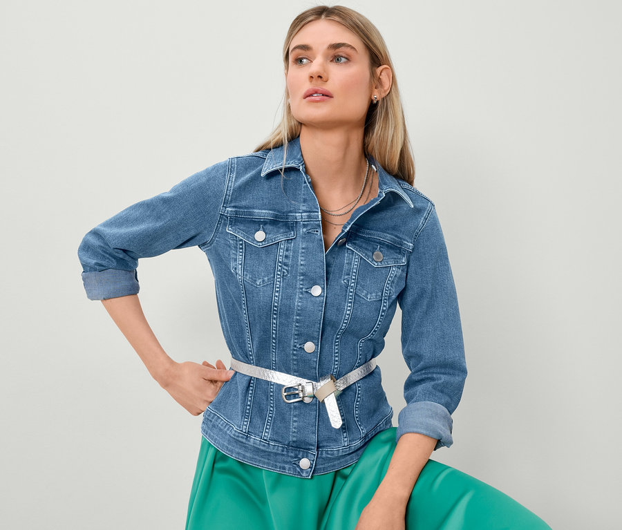 Blond nő farmerdzsekiben és szaténszoknyában pózol.