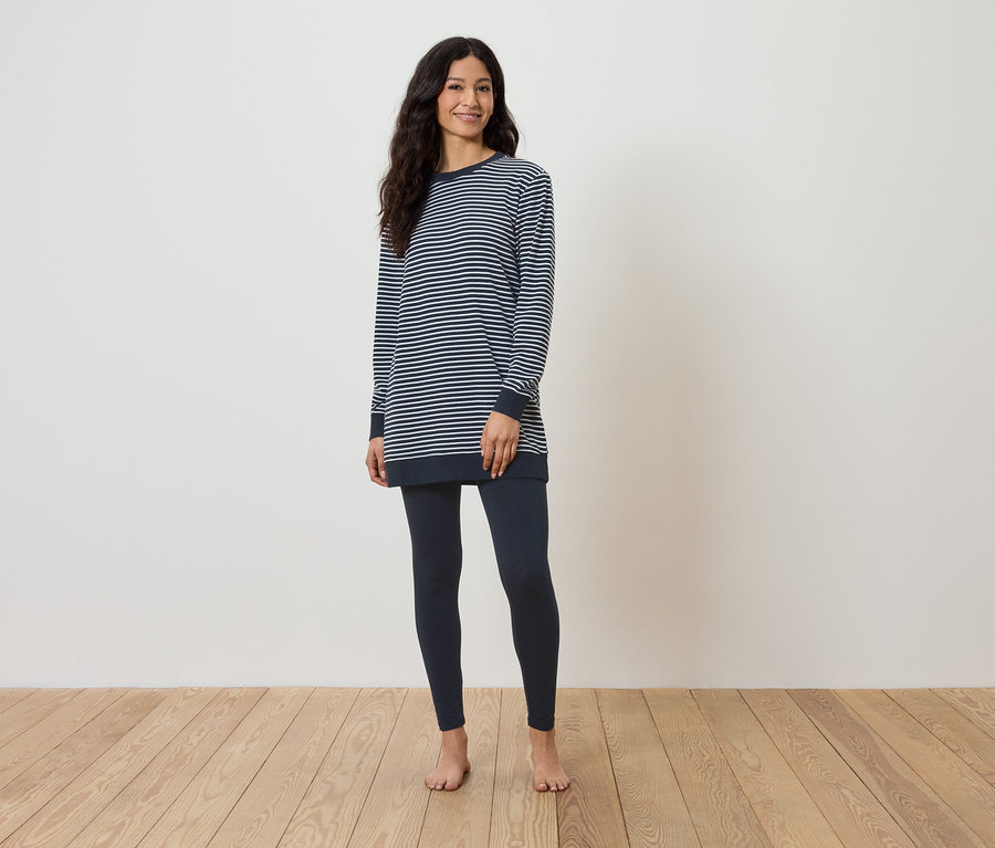 Egy nő mezítláb áll a fapadlón, csíkos, hosszú ujjú felsőt és sötétkék leggingset visel.