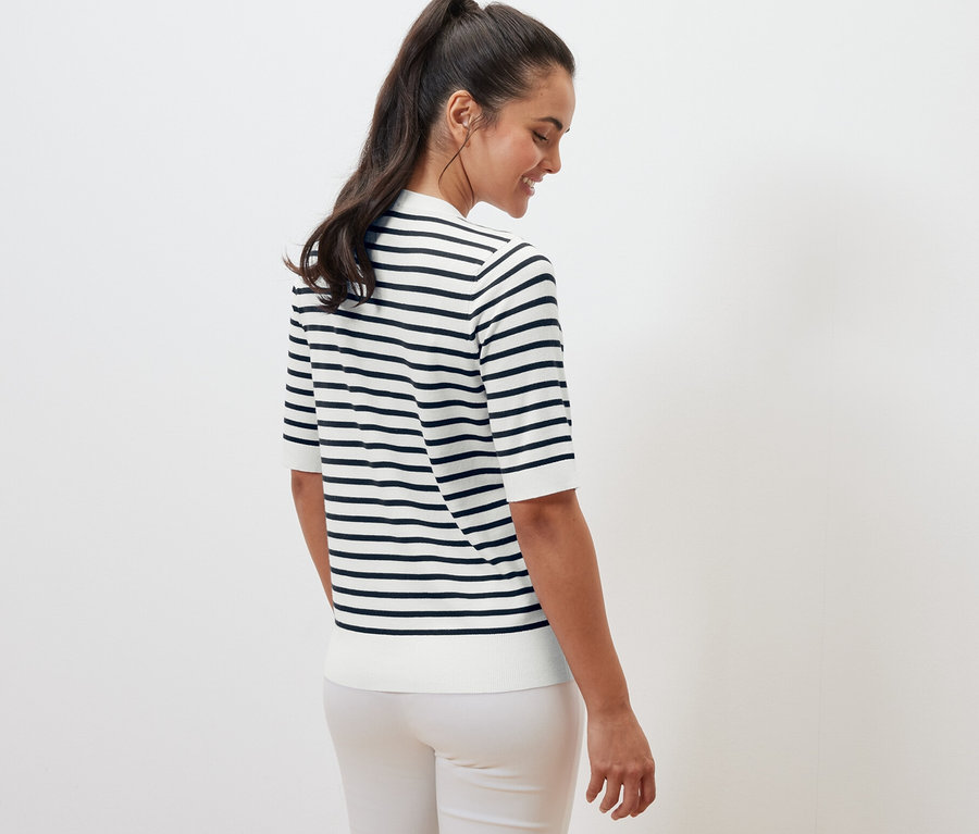 Hátulról látható nő tengerészkék, finom kötésű, csíkos pulóvert visel.