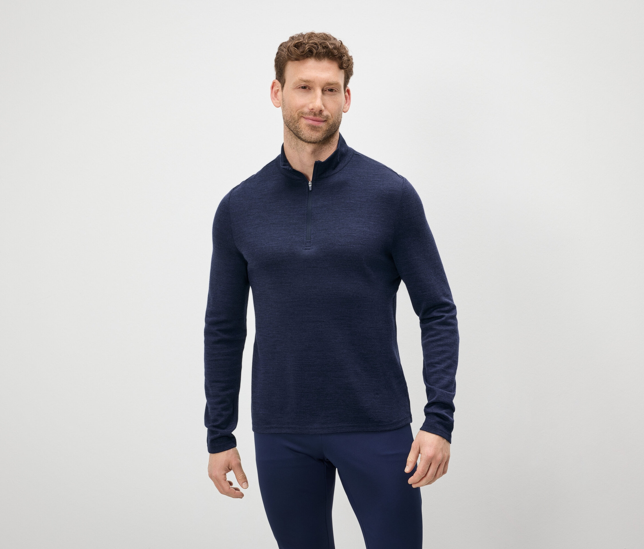 Barna hajú és szakállú férfi kék cipzáras pulóvert és kék nadrágot visel.