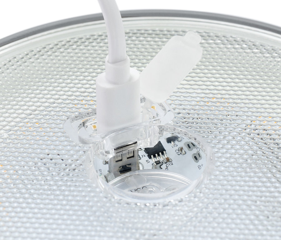 Közeli kép egy fehér USB csatlakozóról, amely egy átlátszó aljzatba van bedugva, látható elektronikus alkatrészekkel.
