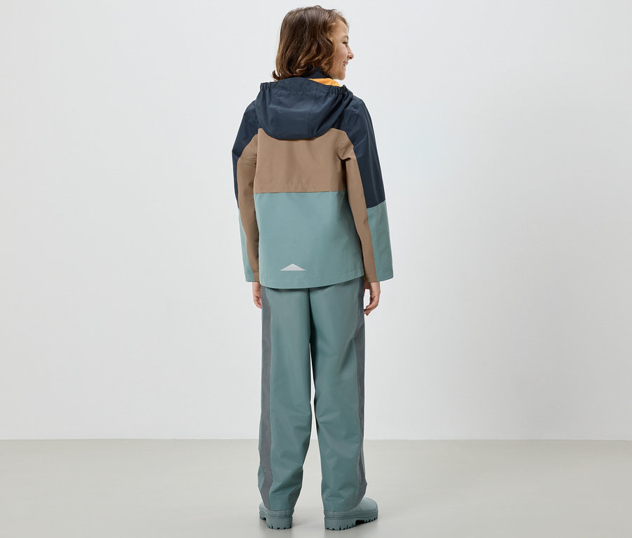 Egy lány hátulról színes kabátban és Kinder-Regenhose, salbei nadrágban.