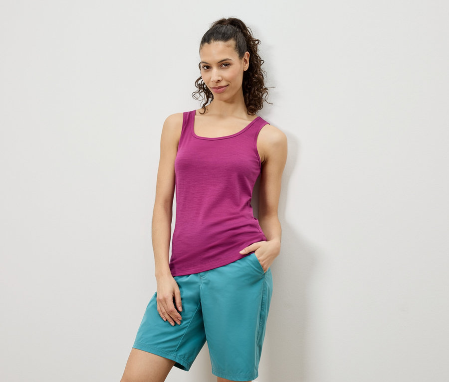 Nő pózol rózsaszín trikóban és türkiz rövidnadrágban egy fehér fal előtt.