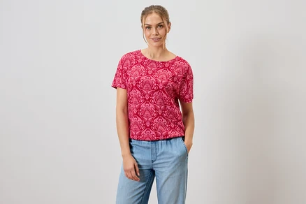 Frau trägt ein rotes, gemustertes T-Shirt und blaue Jeans.