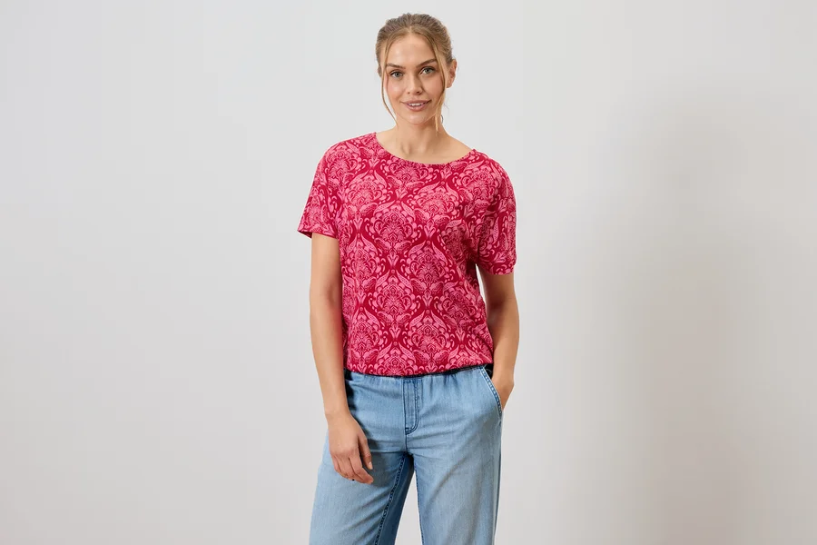 Frau trägt ein rotes, gemustertes T-Shirt und blaue Jeans.