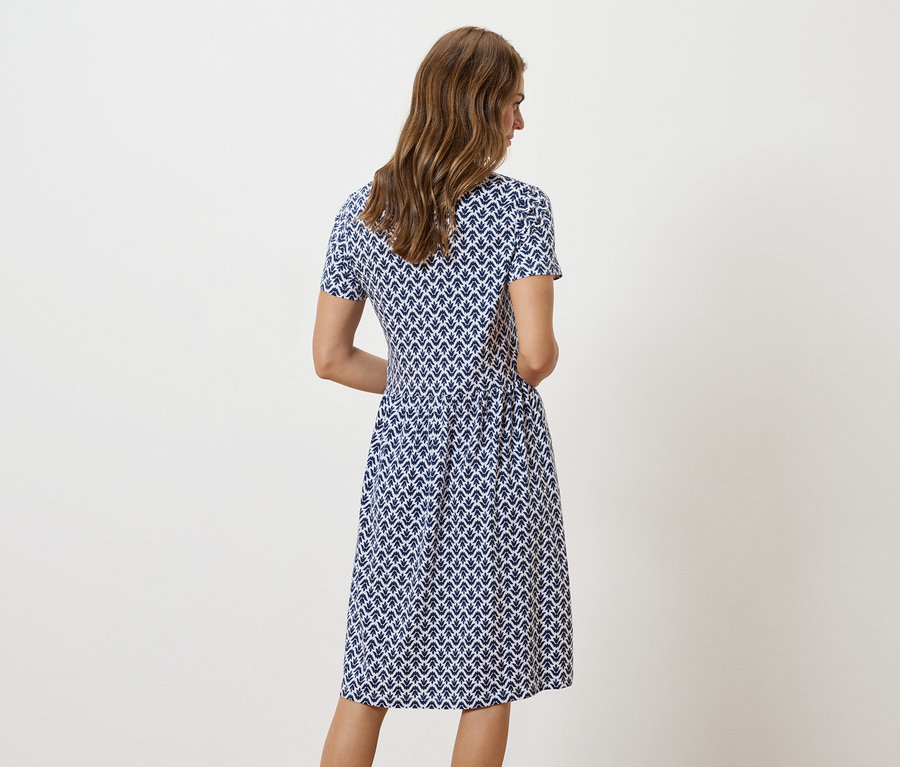 Egy nő áll háttal a kamerának, kék-fehér mintás ruhát visel.