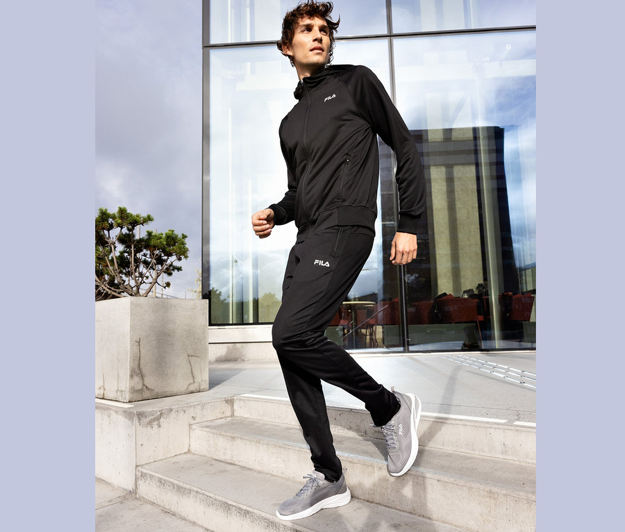 Fekete Fila tréningruhát viselő férfi lépcsőzik lefelé egy betonteraszról, szürke Fila cipőben.