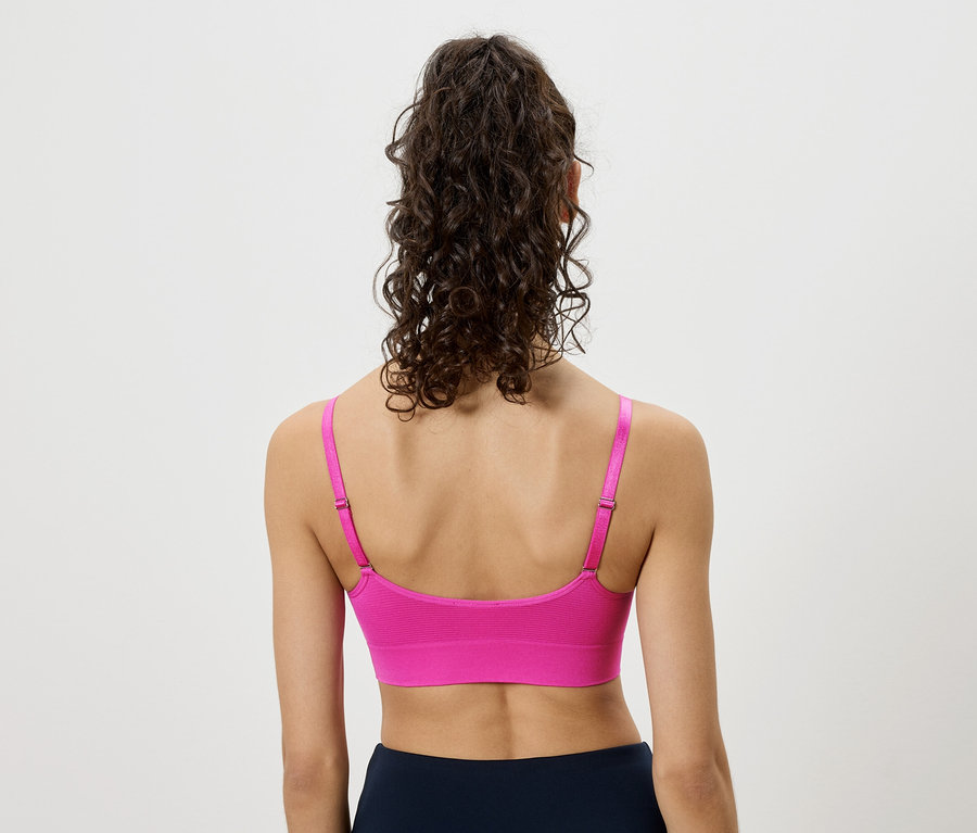 Hátulról látható egy nő, aki göndör haját feltűzte, rózsaszín sportmelltartót és sötétkék leggingset visel.