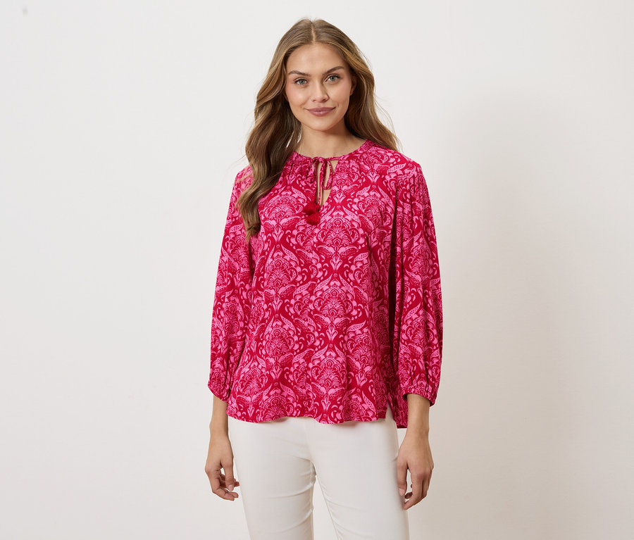 Nő visel egy mintás rózsaszín blúzt és fehér nadrágot.