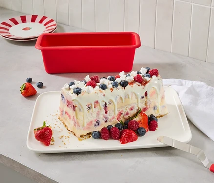 Jeges desszert bogyós gyümölcsökkel egy tányéron, mellette egy piros tortaforma és piros csíkos tányérok.