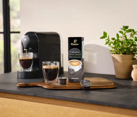 A kávéfőző kávét készít egy pohárba a Cafissimo Caffè Crema – 10 kapszula csomagolása mellett.