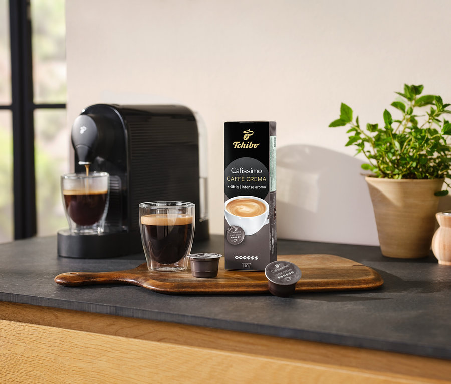 A kávéfőző kávét készít egy pohárba a Cafissimo Caffè Crema – 10 kapszula csomagolása mellett.