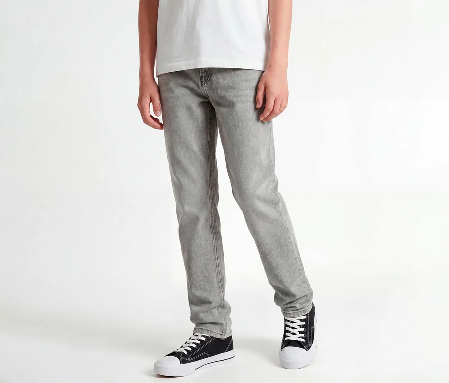 Fehér pólót, szürke Jack&Jones JJOriginal Chris farmernadrágot és fekete sportcipőt viselő álló személy.